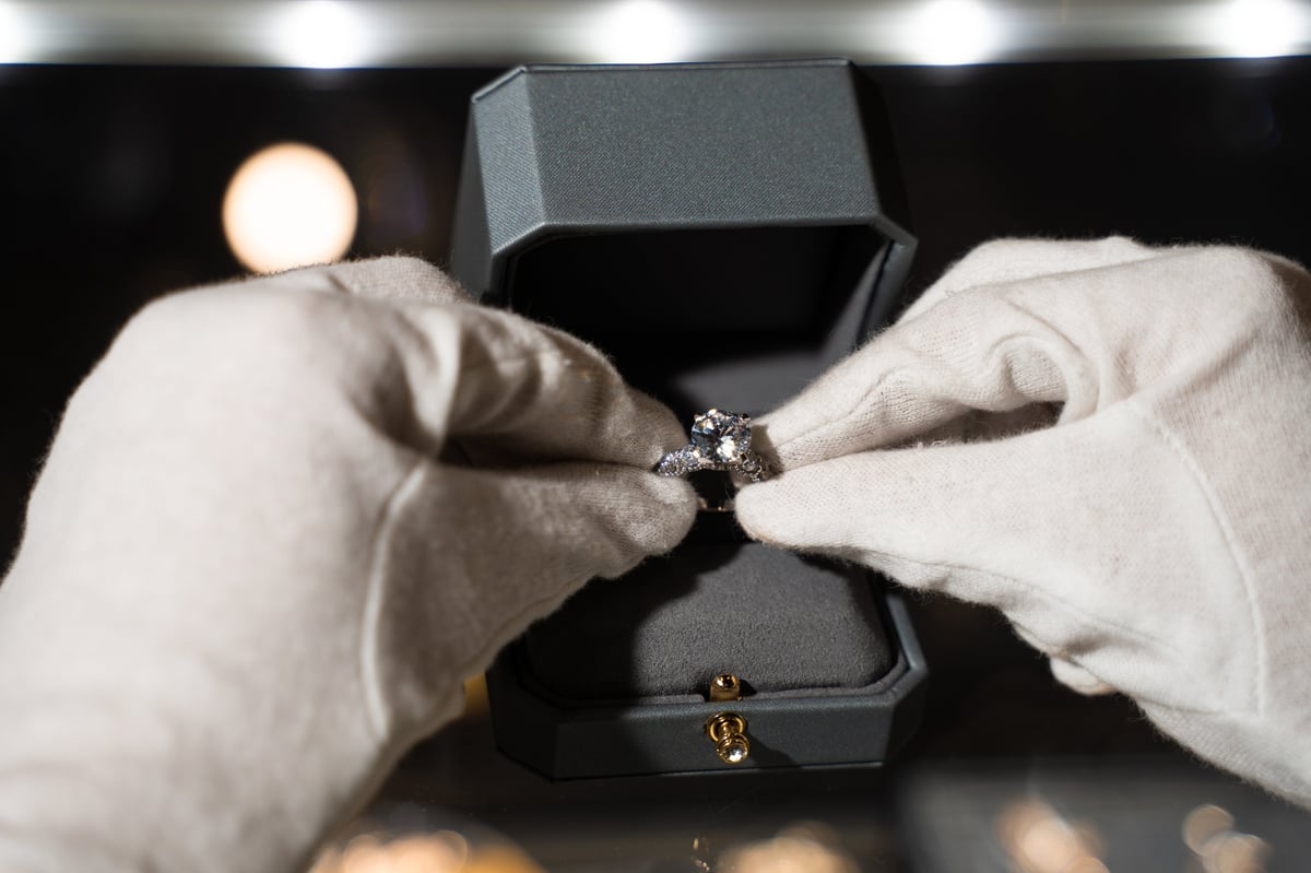 A jeweler in white gloves placing an engagement ring into a jewelry box